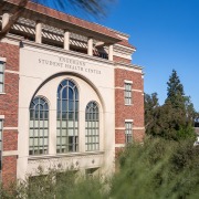 The front of the Engemann Health Center, a red brick building with a cream-colored center. Above the three tall rectangular windows in the cream-colored center of the facade is the text "Engemann Student Health Center."