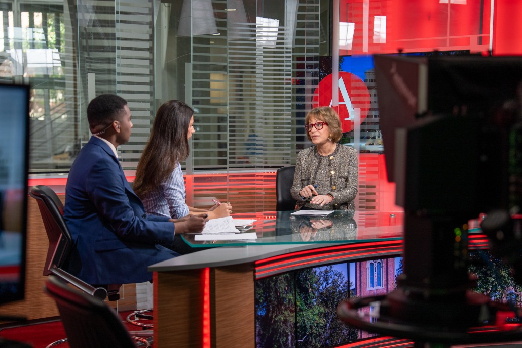 Carol Folt sits across from two student journalists. A camera is on the right side of the image.