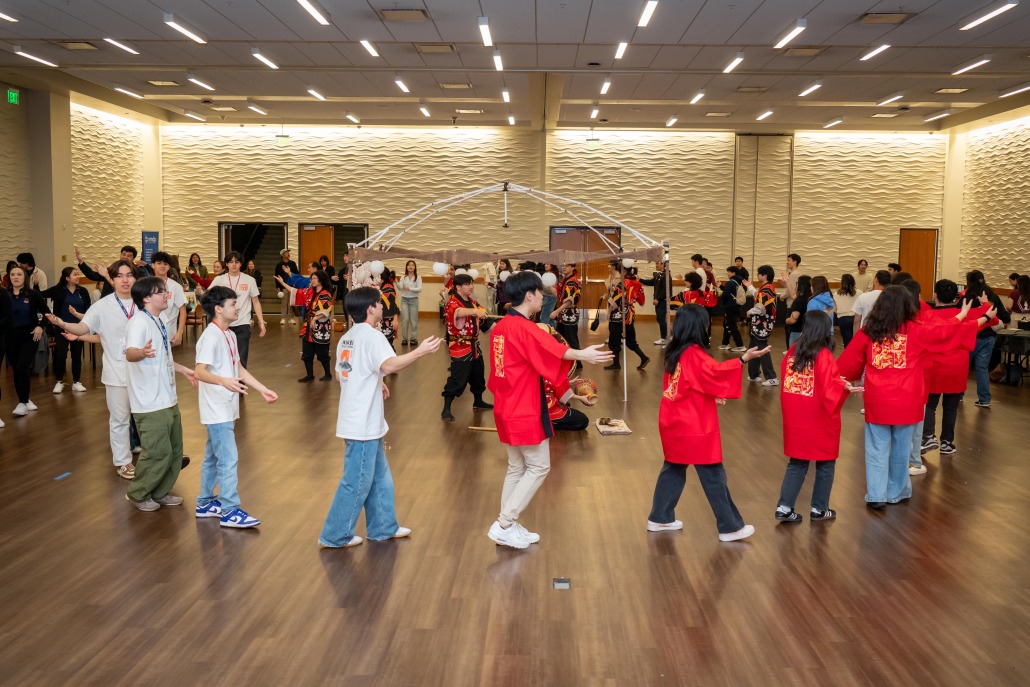 Students dressed in red or white clothing dance in a circle.