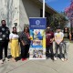 Individuals from the USC Schwarzenegger Institute stand beside a poster for the Altadena Arts Magnet School with a bottle of the MacSchwarzenegger whiskey.