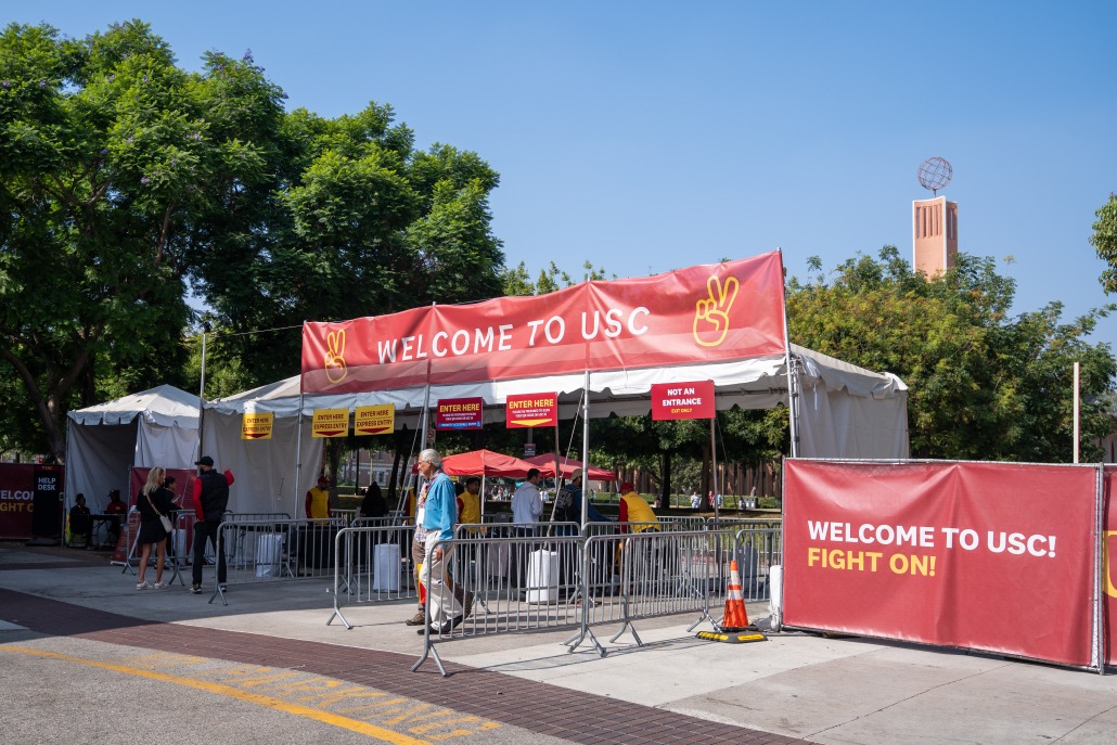 The front of the McCarthy Way entrance. A man wearing a blue jacket exits, and a sign above the tent containing the security scanners reads "Welcome to USC." To the right side of the tent, a sign reads, "Welcome to USC! Fight on!"