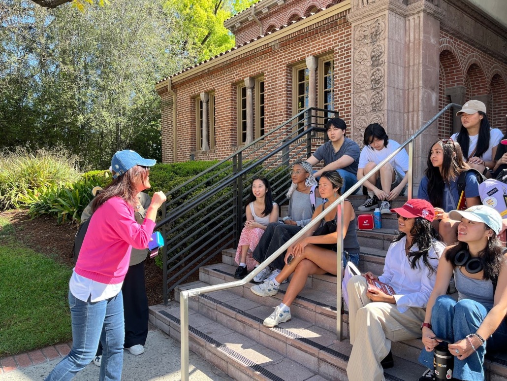Students sit on the stairs outside the Amy King Dundon-Berchtold University Club. On the left, an organizer speaks to the students.
