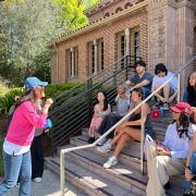 Students sit on the stairs outside the Amy King Dundon-Berchtold University Club. On the left, an organizer speaks to the students.