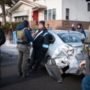 Immigration enforcement agents question man in front of a crashed car.