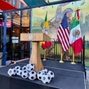 A podium stands before the L.A., U.S. and Mexican flags, with a pile of soccer balls.