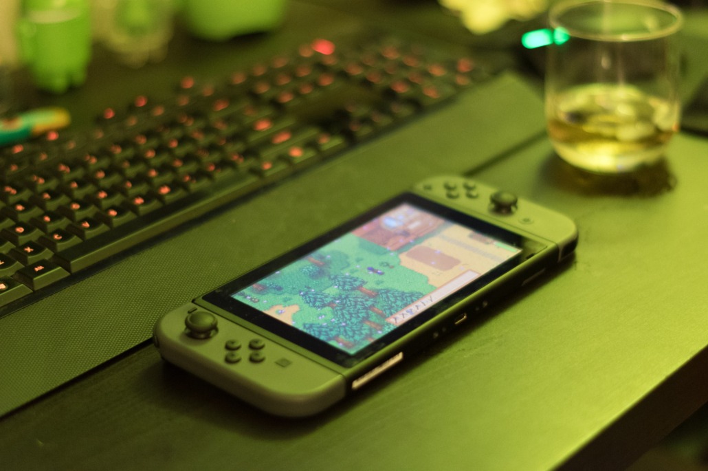 A green Nintendo Switch with Stardew Valley playing sits on a green table.