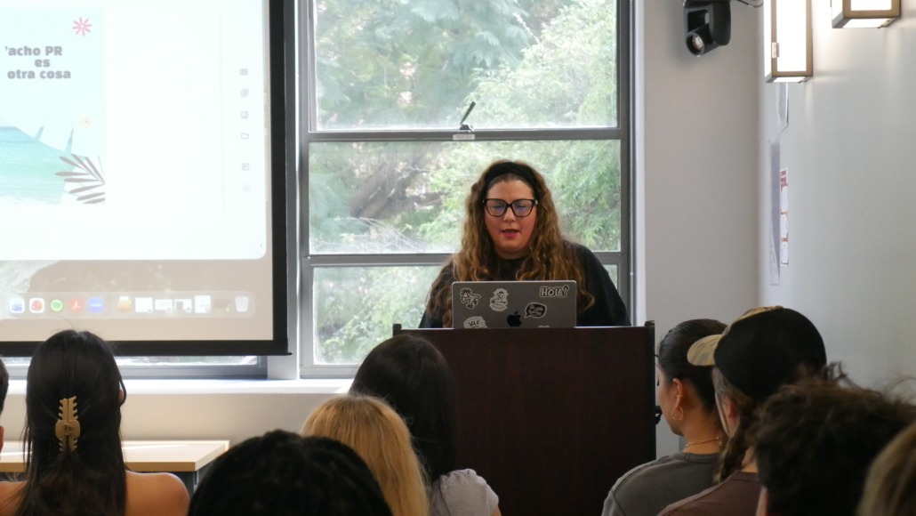 A professor stands at the front of a classroom in front of a projector screen