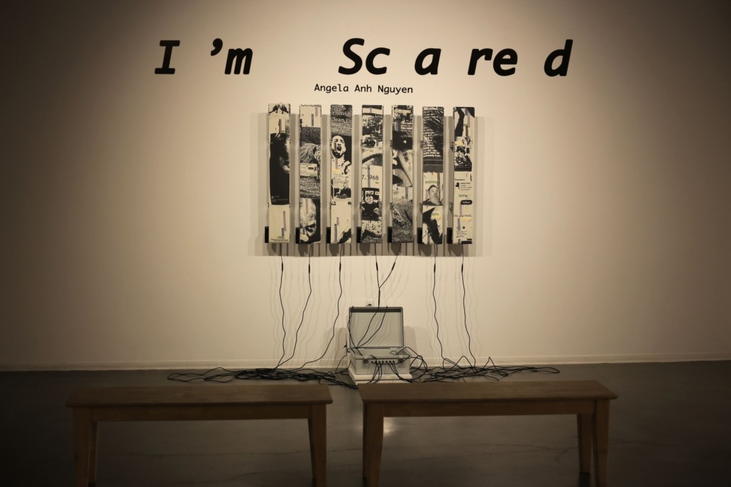 Seven strips of black-and-white rug hung on a wall. Wires connect the bottom of the strips to a gray briefcase