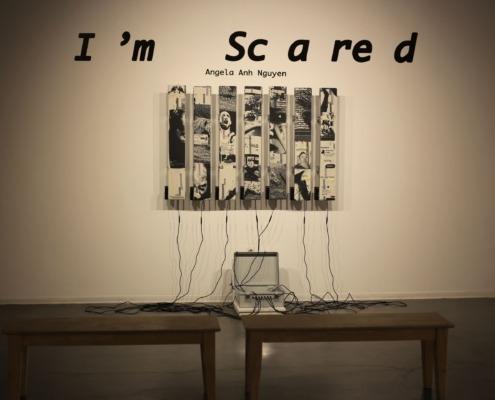 Seven strips of black-and-white rug hung on a wall. Wires connect the bottom of the strips to a gray briefcase