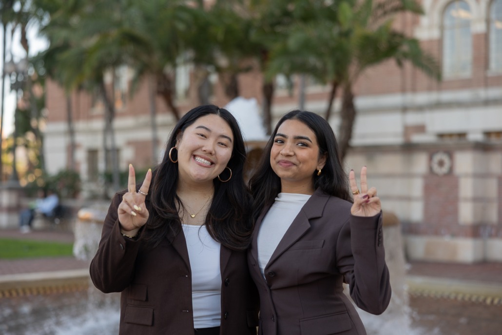 Two women wearing brown suit jackets stand on USC's campus
