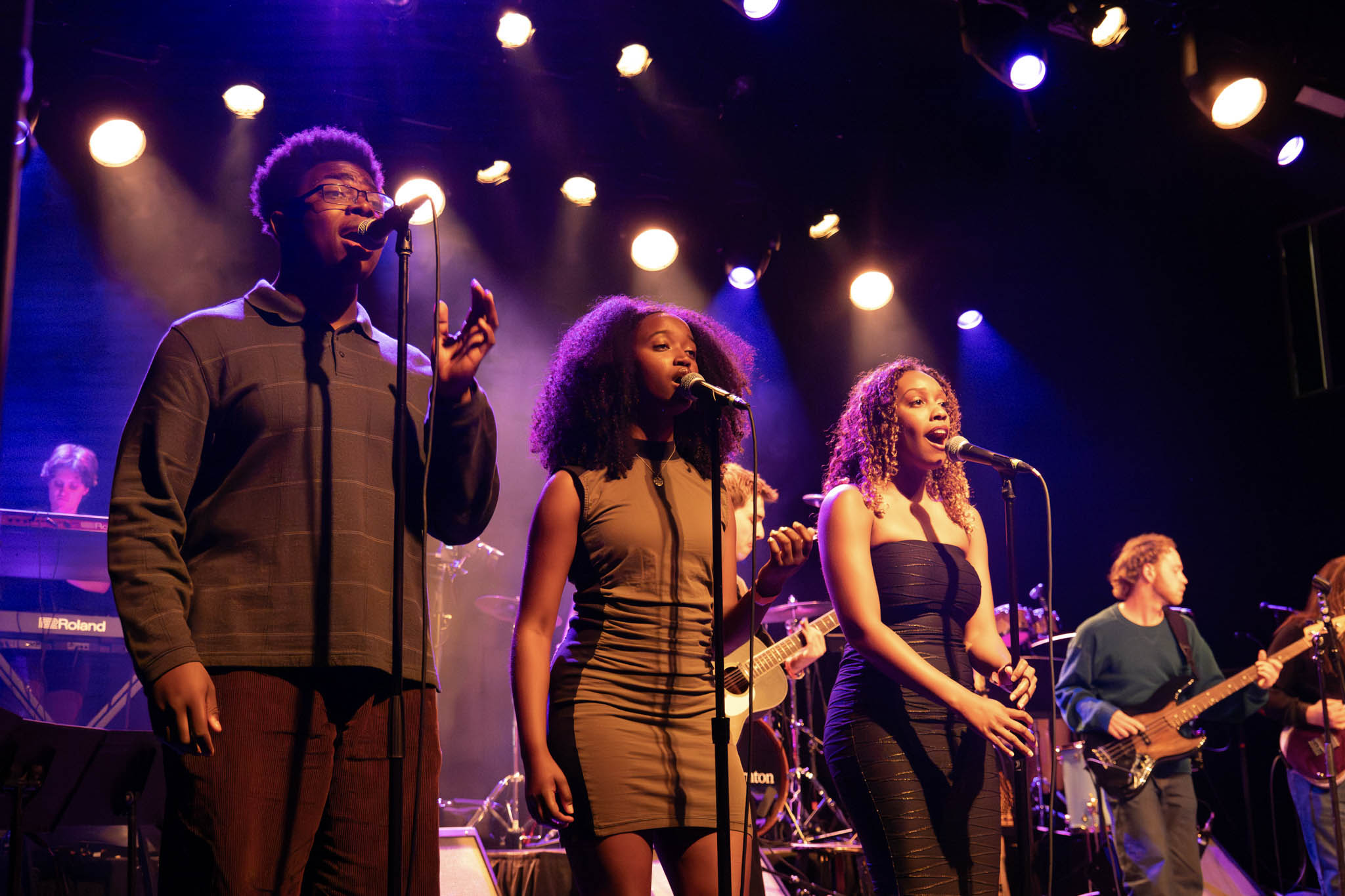 Three singers perform on stage together at the pop showcase.