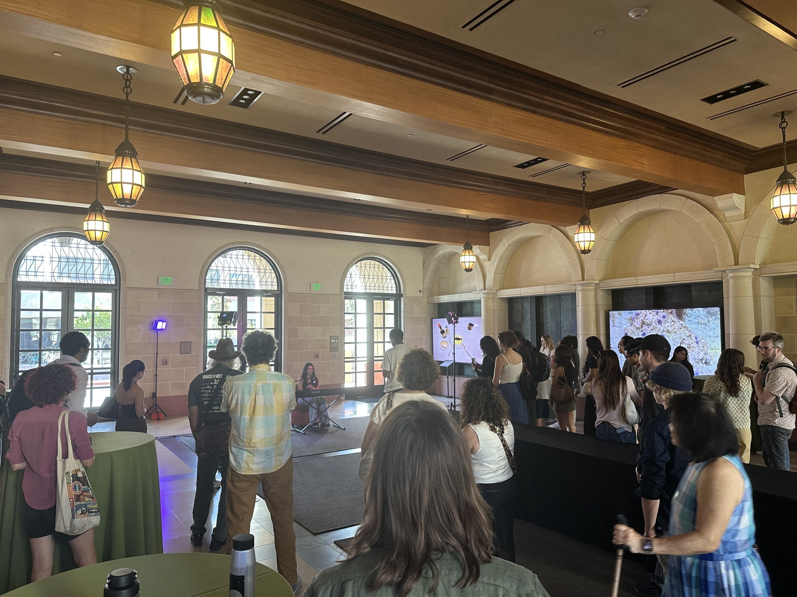 Attendees gather in the lobby of the building to watch a piano performance.