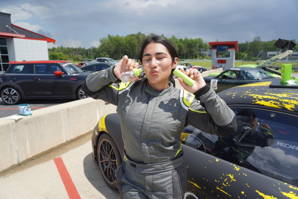 student founder sprays her skincare on her face in front of her racecar
