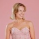 Mia Lind poses wearing a pink dress in front of a pink backdrop.