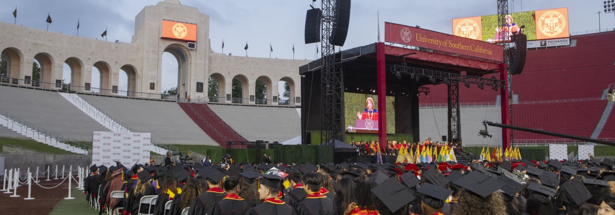 USC students in caps and gowns sit on the field of the Coliseum at the commencement ceremony.