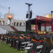 USC students in caps and gowns sit on the field of the Coliseum at the commencement ceremony.
