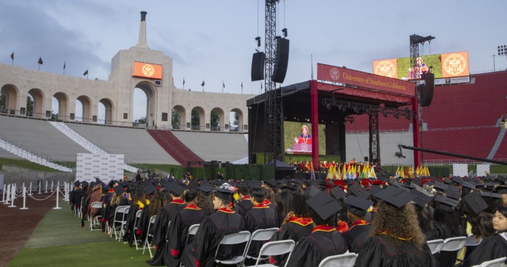 USC students in caps and gowns sit on the field of the Coliseum at the commencement ceremony.