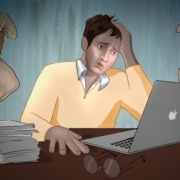 A man in a yellow sweater next to a computer being stressed about money