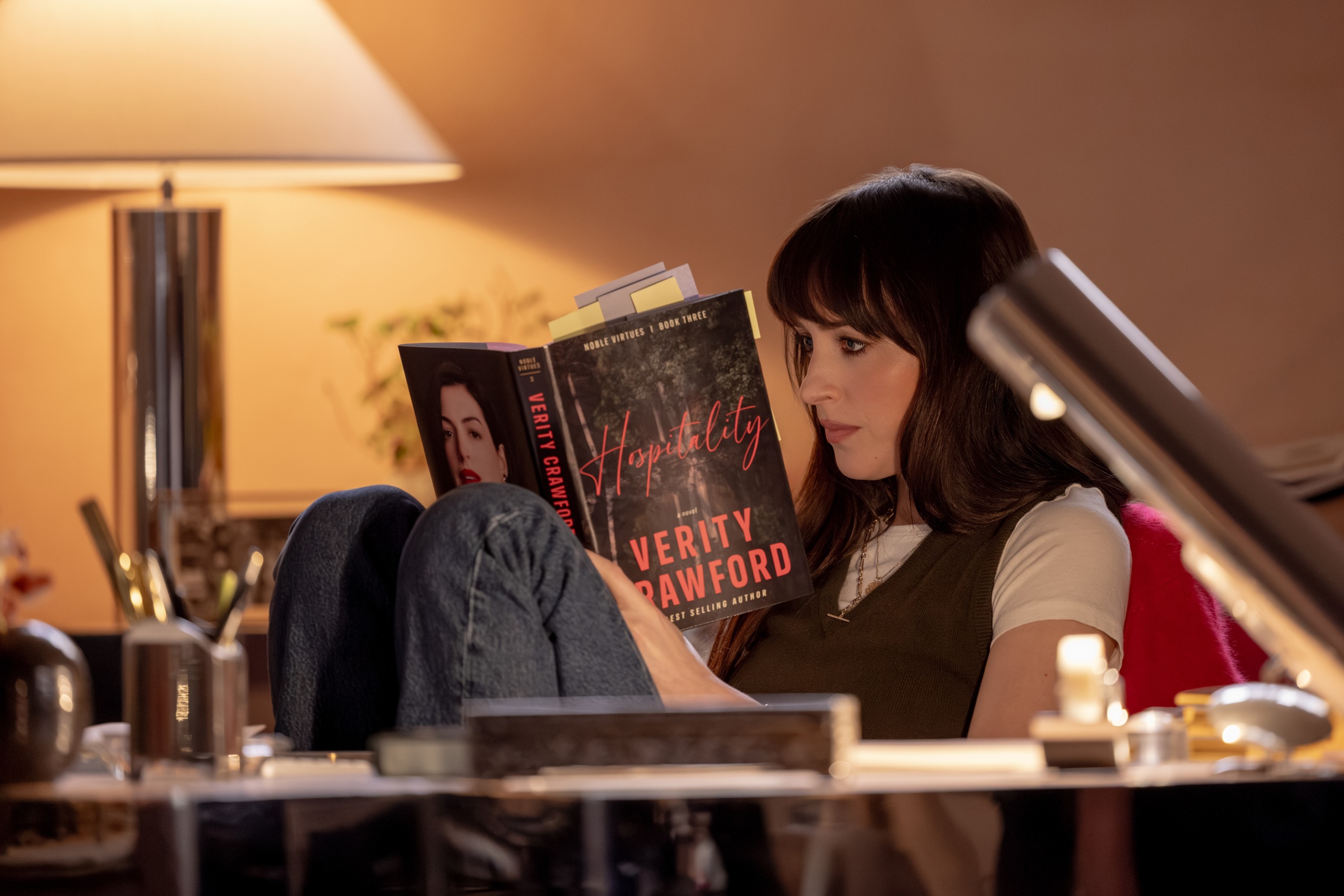Lowen (Dakota Johnson) reads one of Verity's (Anne Hathaway) books.